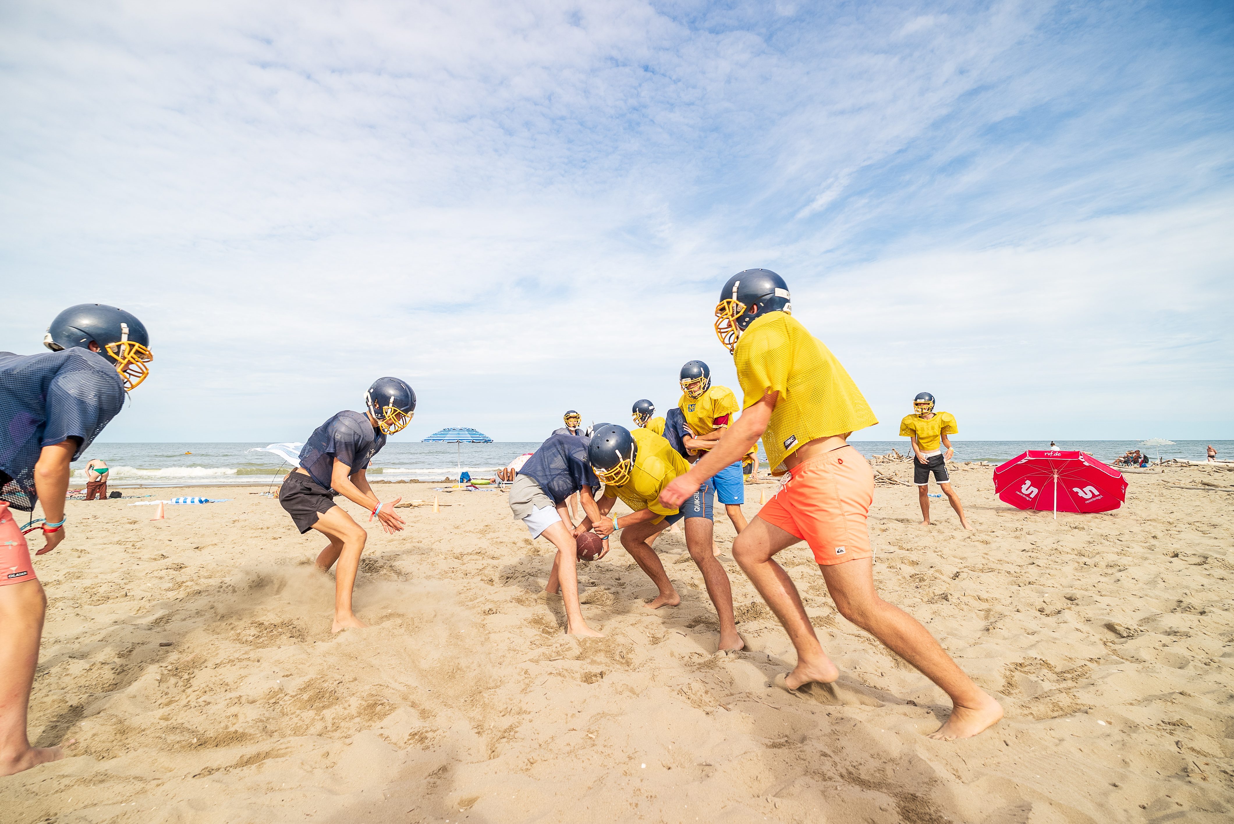 Gäste spielen American Football am Strand und tragen dabei Helm und Schulterpolster