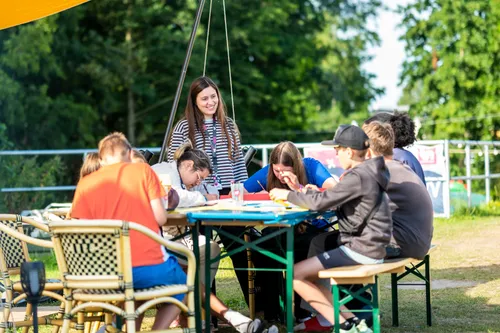 Teamer:innen sitzen mit Gästen an einem Tisch und Basteln